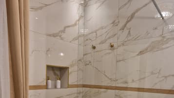 Ein modernes Badezimmer mit Duschkabine aus Glas, Marmorwänden, Holzboden und Waschbecken in Weiß.