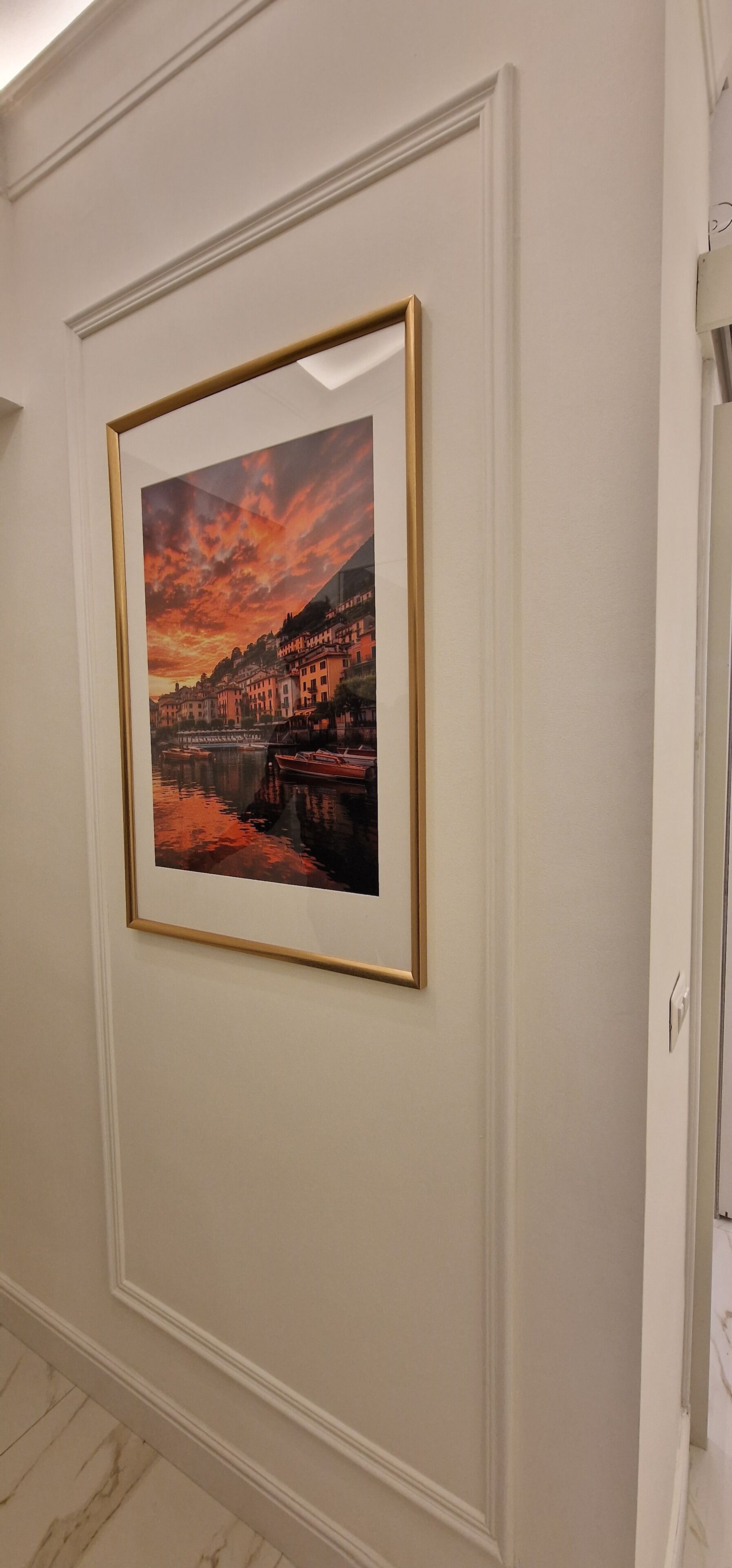 A framed picture of a sunset over a coastal town on a wall.