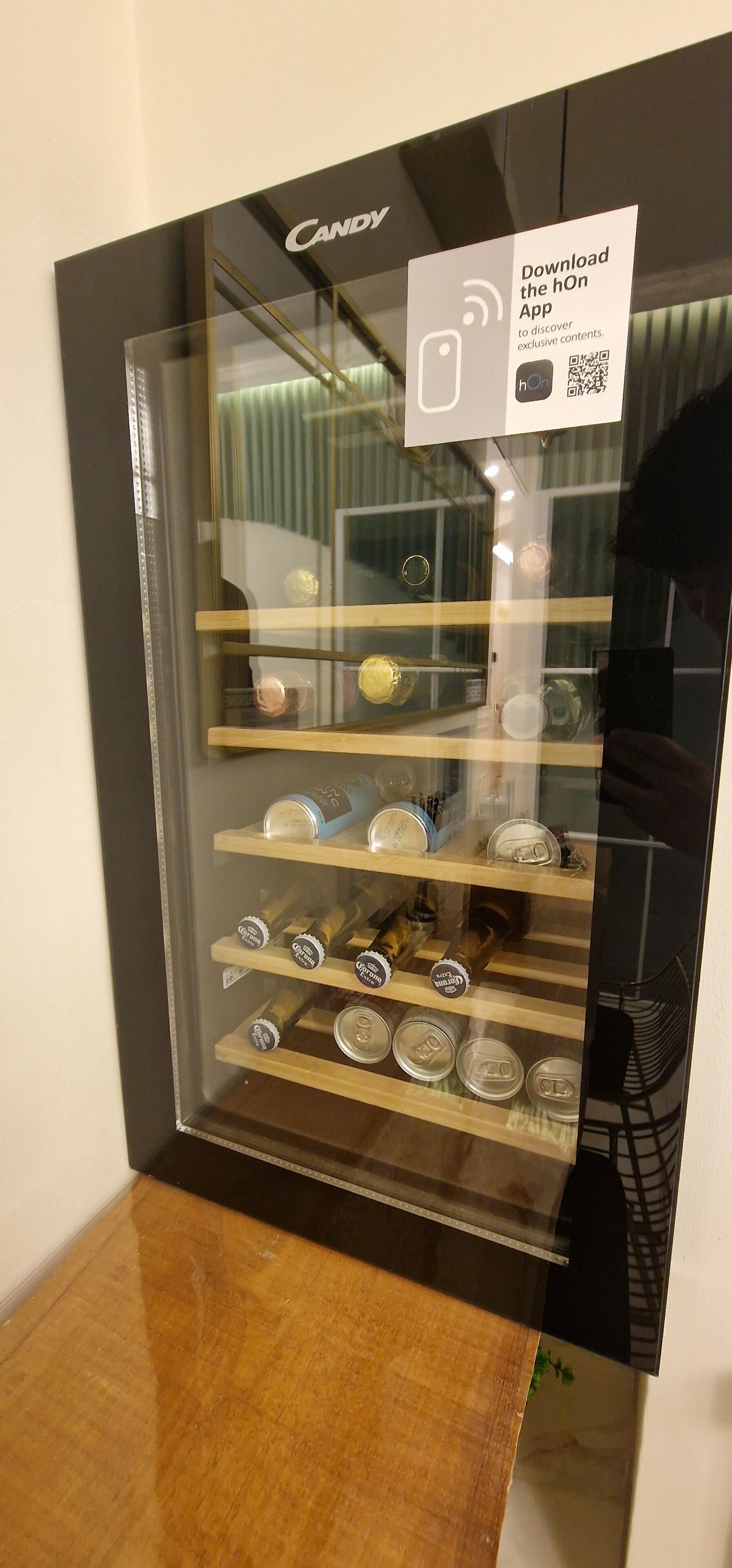 A display case with various cans, including Corona, and a sign promoting the hOn App.
