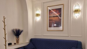 Una sala de estar moderna con un sofá azul, un cuadro en la pared y dos lámparas fijadas a la pared.