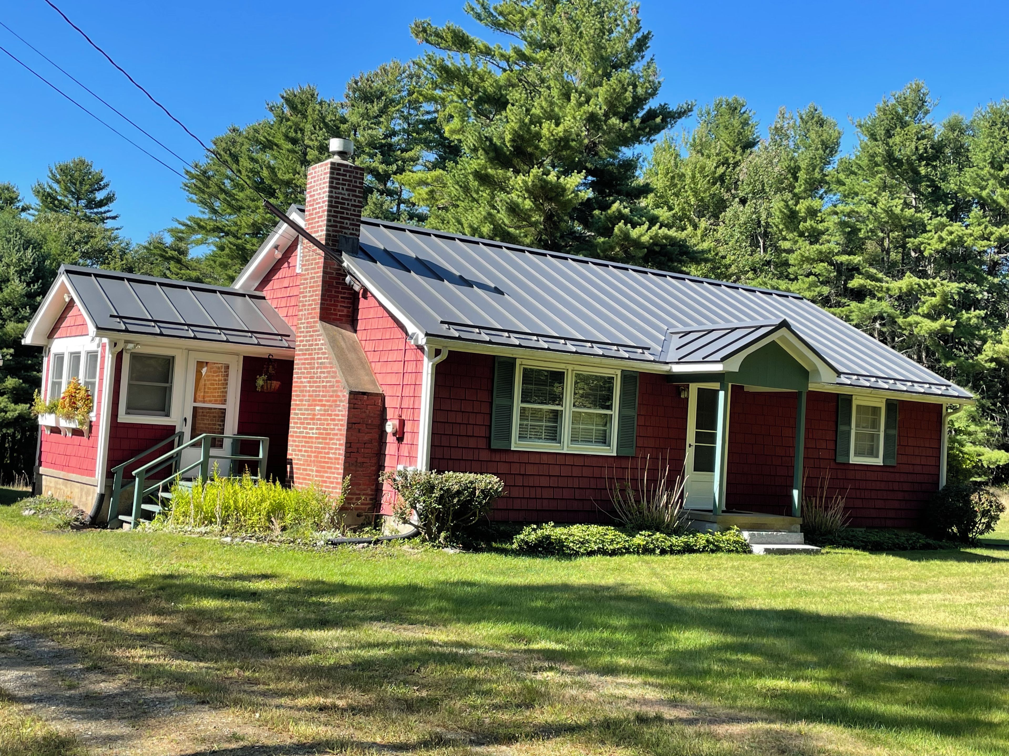 A single-story house with a brick exterior, a metal roof, and a front porch.