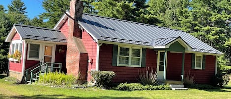 A single-story house with a brick exterior, a metal roof, and a front porch.
