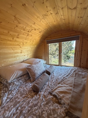 A cozy wooden cabin bedroom with a bed, pillows, and a window overlooking trees.