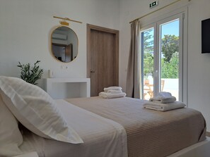 A bedroom with a bed, a bedside table, a mirror, a door, and a view through a window. - ALINTHEA 1, Alinda, Leros (Leros)