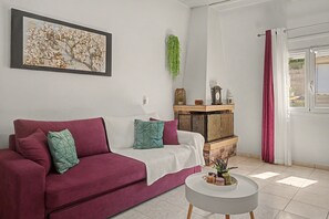 Ein Wohnzimmer mit einer Couch, einem Couchtisch, einem Wandbild, einer hängenden Pflanze und einem Fenster mit Vorhängen.