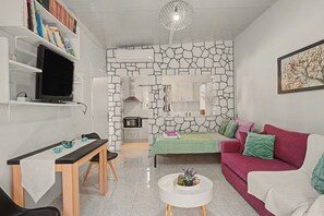A modern living room with a stone wall, a red sofa, a white coffee table, and a television on a shelf. - Holiday Home 'Domenica Apartment' with Mountain View, Wi-Fi and Air Conditioning (Salamina)