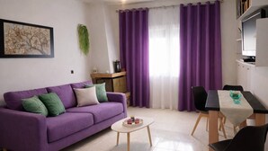 A living room with a purple sofa, a small round table, a dining table with chairs, and purple curtains. - Holiday Home 'Domenica Apartment' with Mountain View, Wi-Fi and Air Conditioning (Salamina)