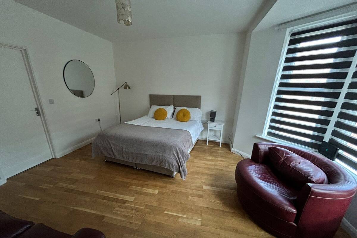 Un dormitorio con cama, mesita de noche, lámpara, silla y ventana con persianas.