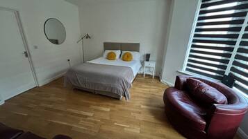 A bedroom with a bed, a nightstand, a lamp, a chair, and a window with blinds.