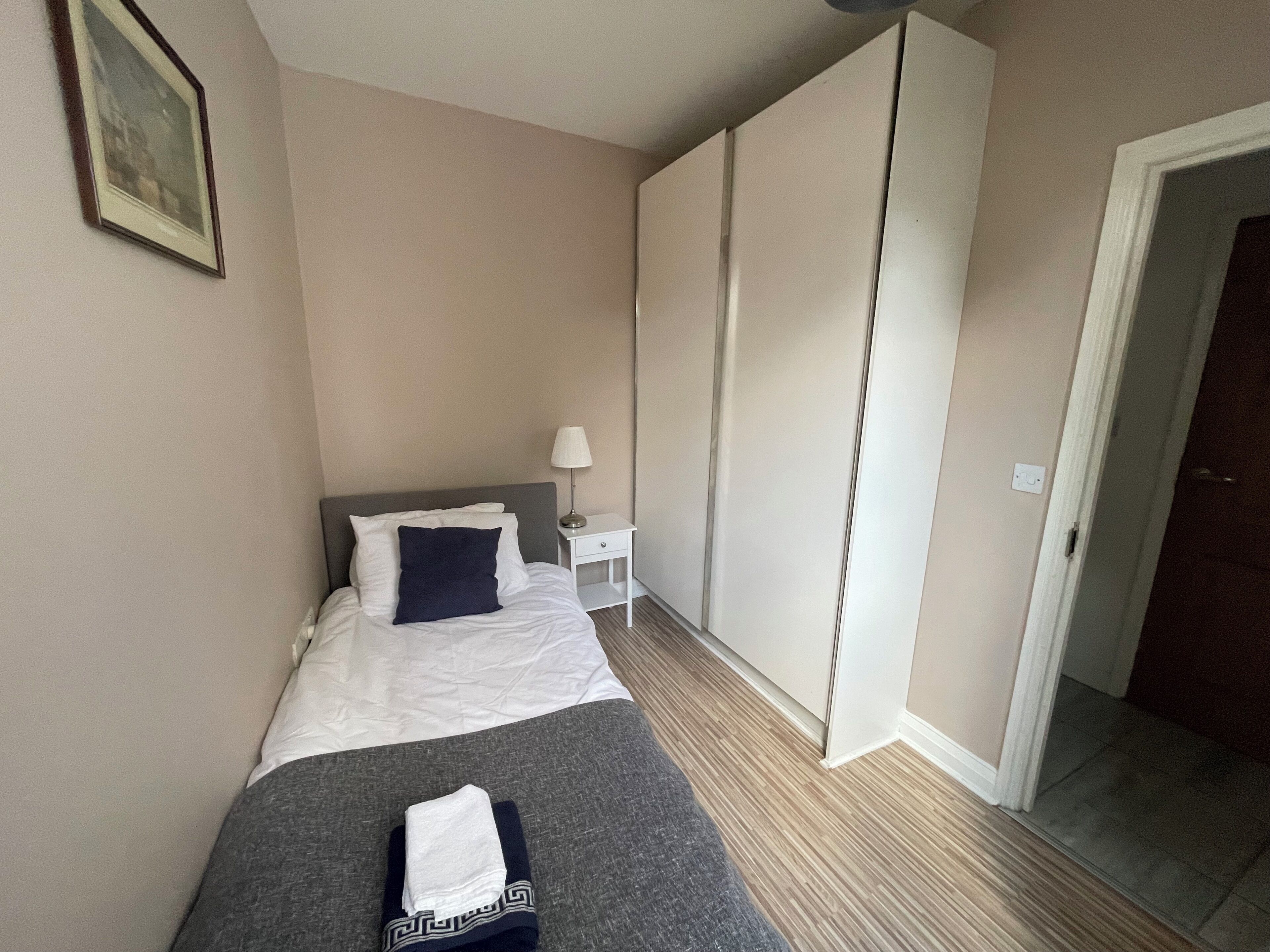 A hotel room with a bed, a nightstand, a lamp, a wardrobe, and a door.