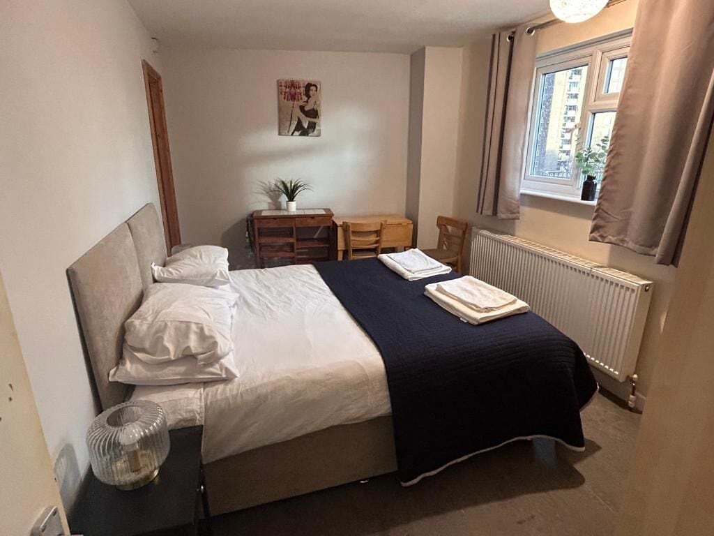 A bedroom with a bed, a desk, a chair, a radiator, and a window with curtains.