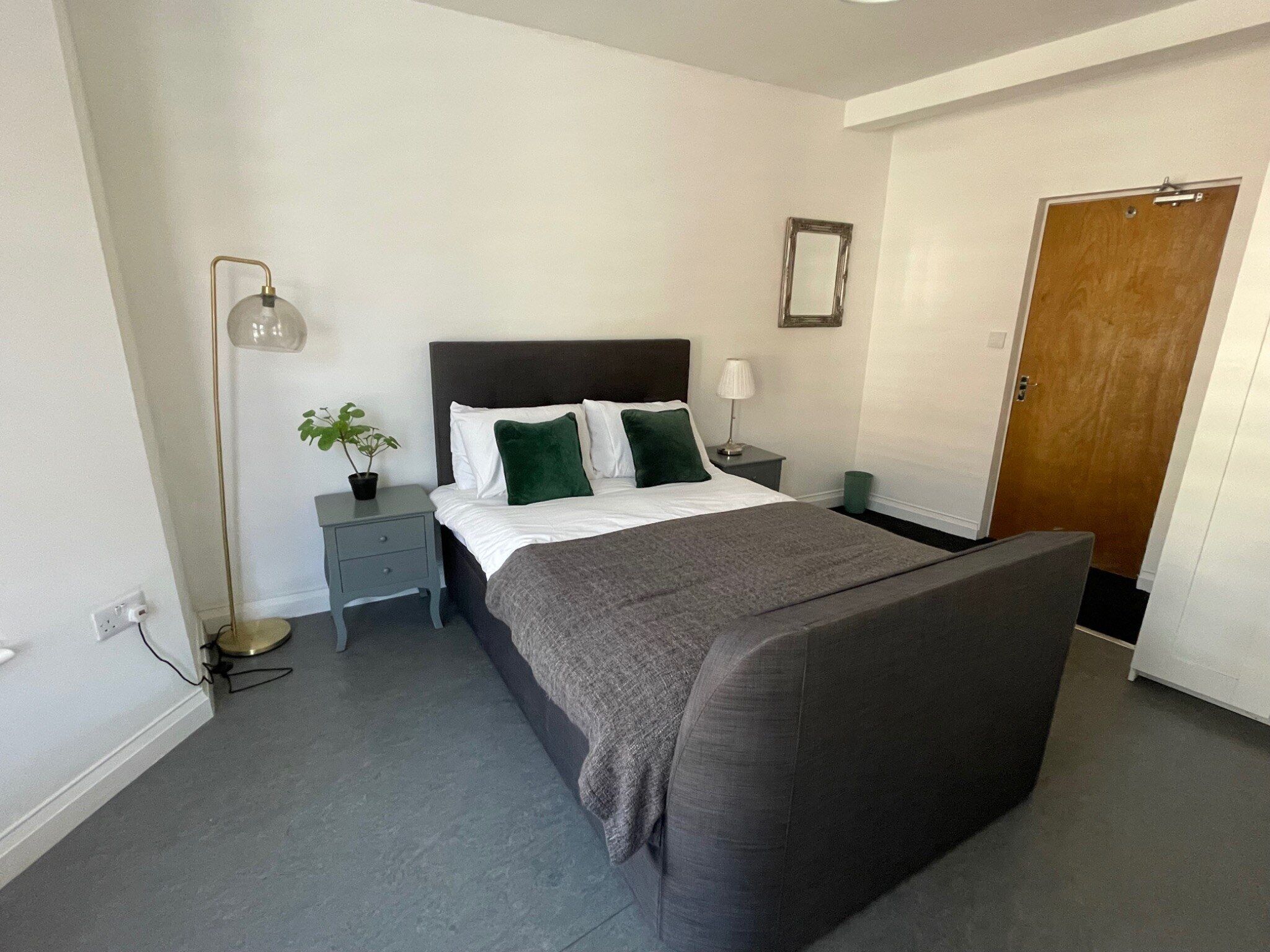 A bedroom with a bed, bedside tables, a lamp, a mirror, and a door.