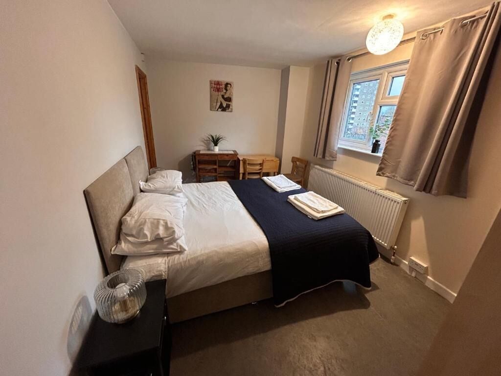 A bedroom with a bed, bedside table, lamp, window, and curtains.