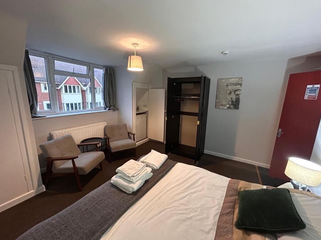 Une chambre d’hôtel avec un lit, deux chaises, une table, une fenêtre donnant sur un paysage agréable, une porte et une lampe.