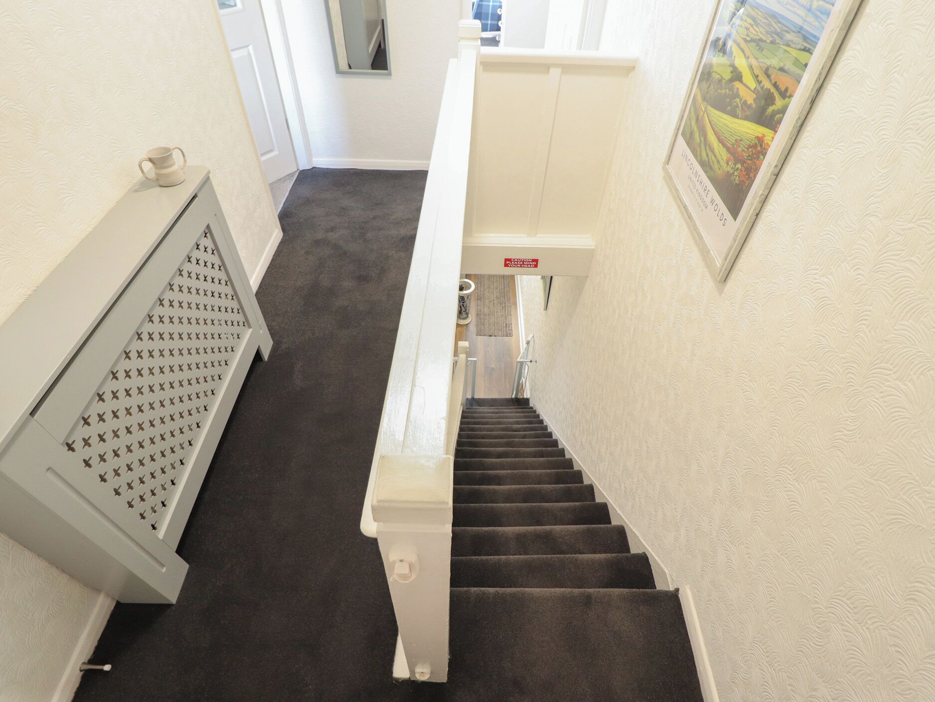 A carpeted staircase with a handrail, a caution sign, and a framed landscape picture on the wall.