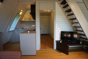 A compact kitchen with a central island, a dining area with a dark wooden table, and a staircase leading to an upper level. - Vacation Home 1 (Kinding - Kratzmühle)