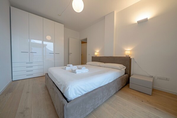 A modern bedroom with a large bed, a wardrobe, and bedside lamps.
