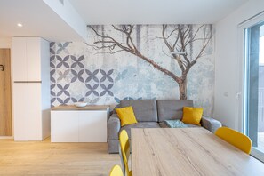 A modern kitchen with white cabinets, a dining table, and a gray sofa with yellow cushions.