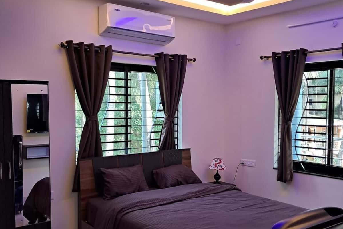 A modern bedroom with a bed, curtains, an air conditioning unit, and a ceiling fan.