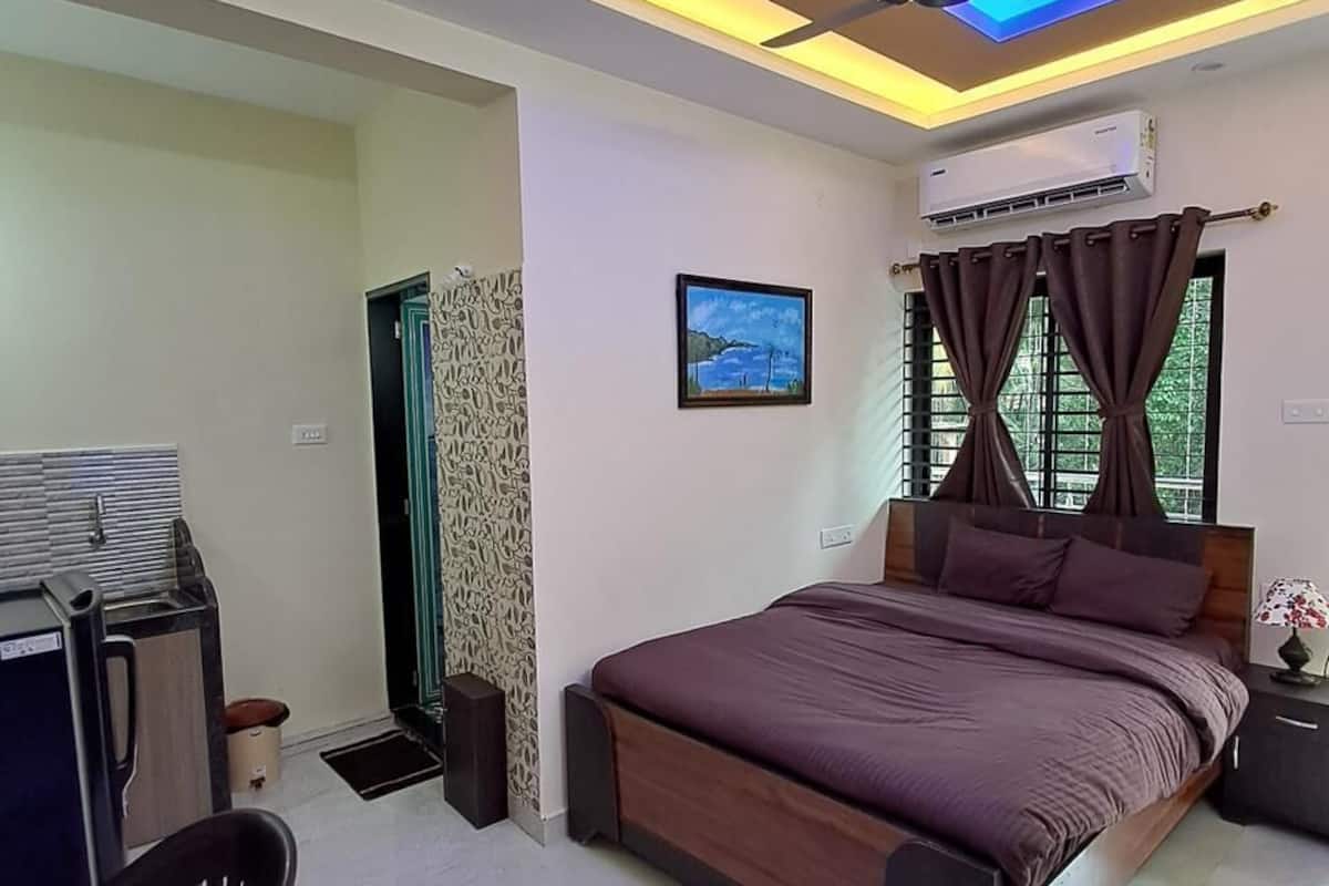 A bedroom with a bed, a ceiling fan, an air conditioning unit, a desk, and a chair.