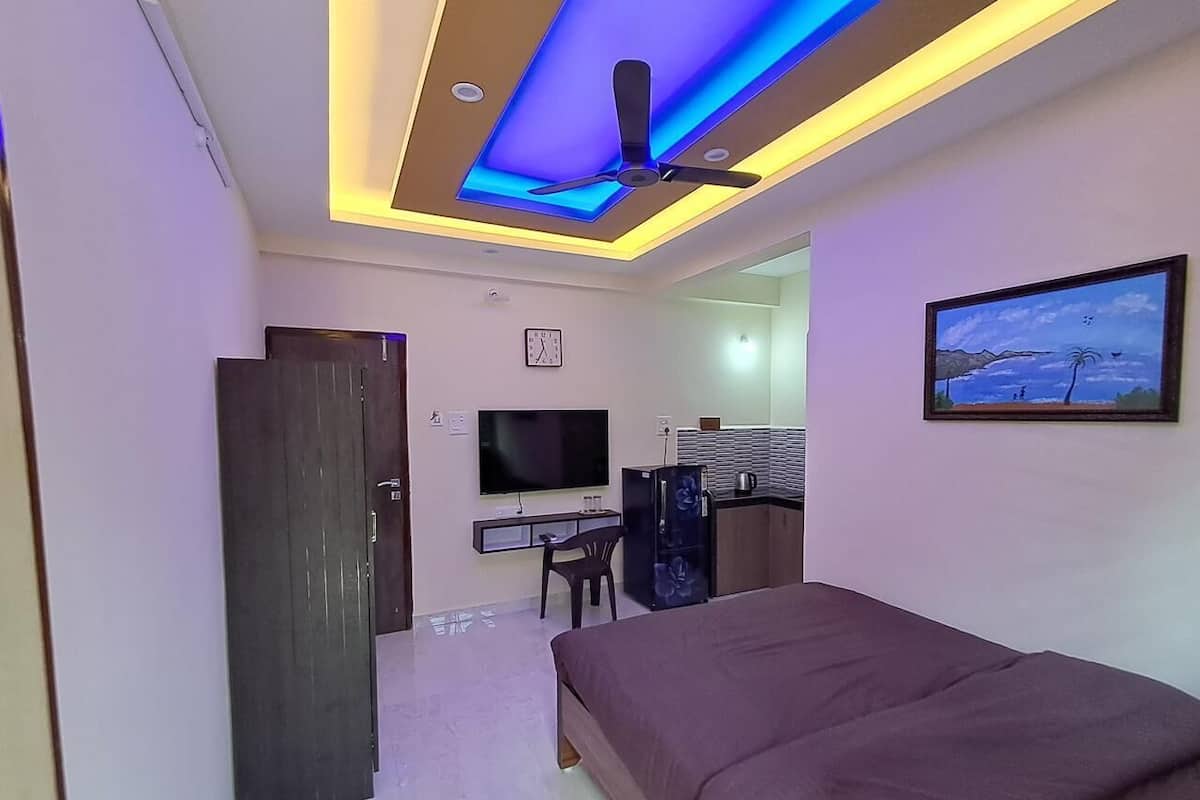 A bedroom with a bed, a desk with a computer, a TV, and a ceiling fan.
