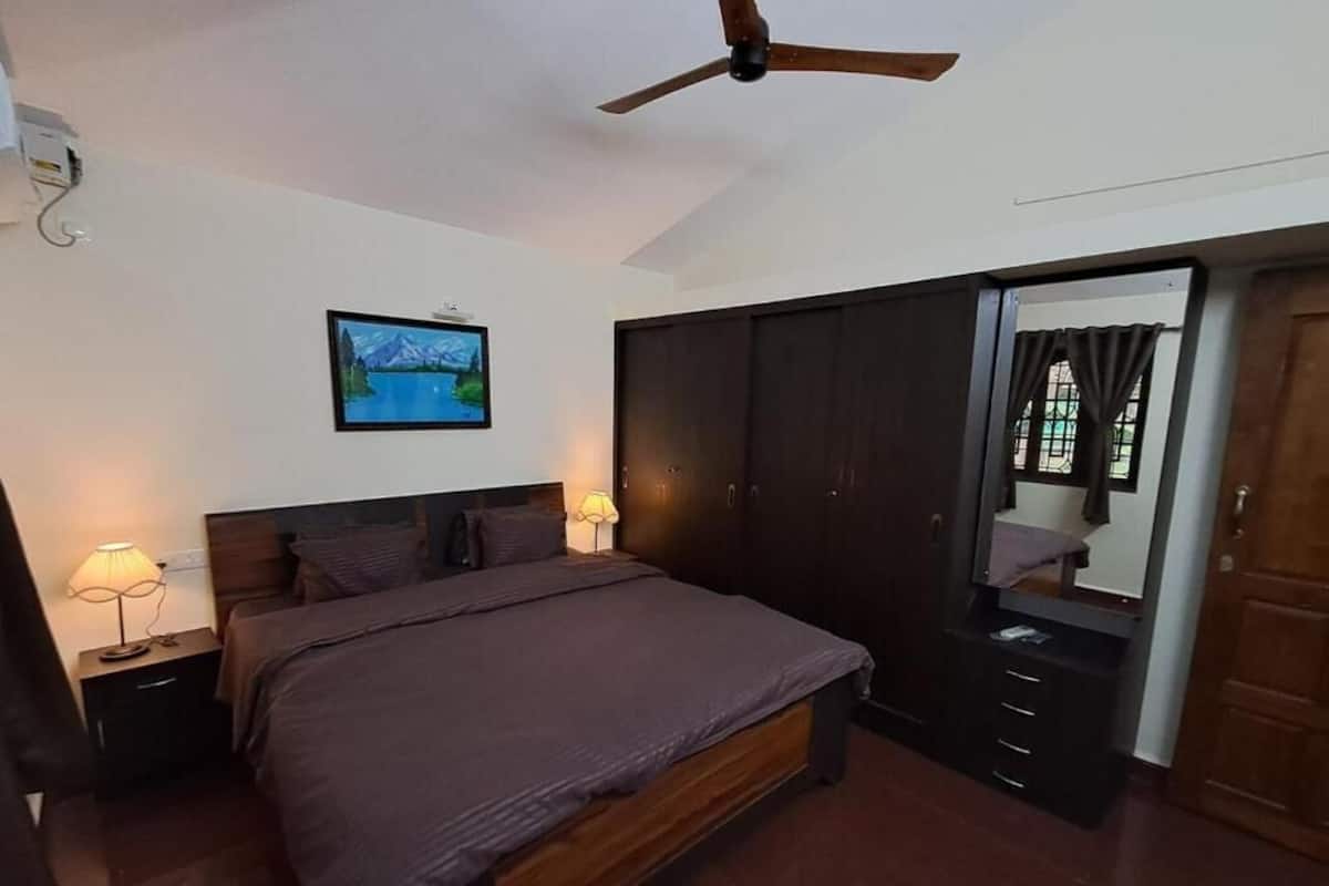 A bedroom with a bed, bedside lamps, a ceiling fan, a wardrobe, and a window with curtains.