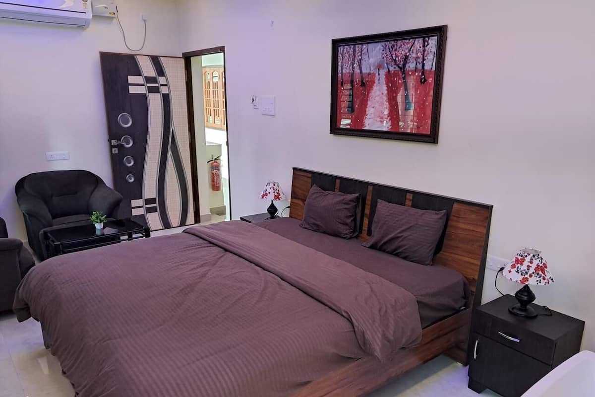 A bedroom with a large bed, a chair, a nightstand, a lamp, and a painting on the wall.