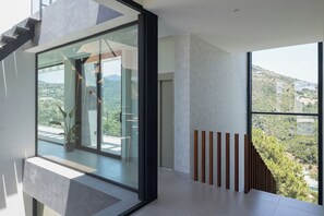 Ein modernes Interieur mit großen Fenstern, einer Treppe und Blick auf eine hügelige Landschaft.