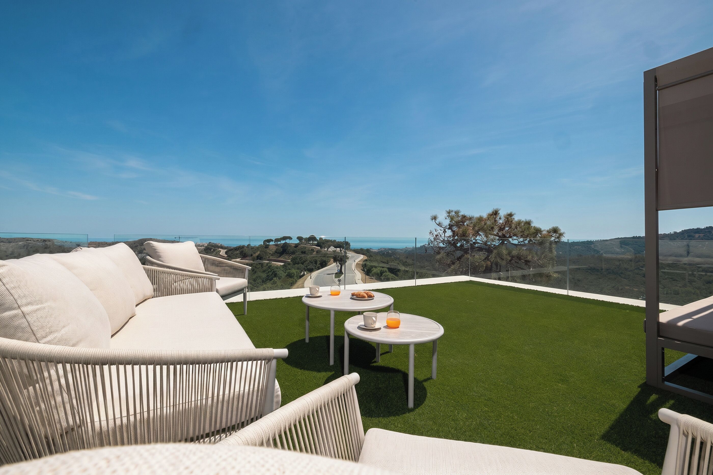 Eine Terrasse mit einer Couch, zwei Tischen und Blick auf die Landschaft.