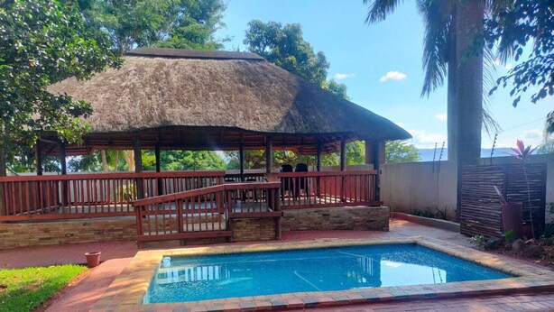 A pool area with a thatched-roof structure, a wooden deck, and a stone wall. - Cozy 1-bedroom lodge in marvelous Sibasa with air conditioning, and a pool (Sibasa)
