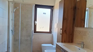 Ein Badezimmer mit Dusche, Toilette und Waschbecken, Holzschränken und einem Fenster.