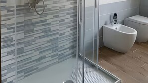 Ein modernes Badezimmer mit einer einteiligen Glasdusche, einer Toilette und einem Bidet.