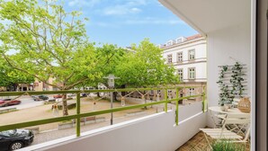 Ein Balkon mit Blick auf eine Straße, einem Tisch mit Stühlen und einer hängenden Pflanze.
