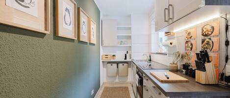 A modern kitchen with white cabinets, a wooden countertop, and framed artwork on the wall.