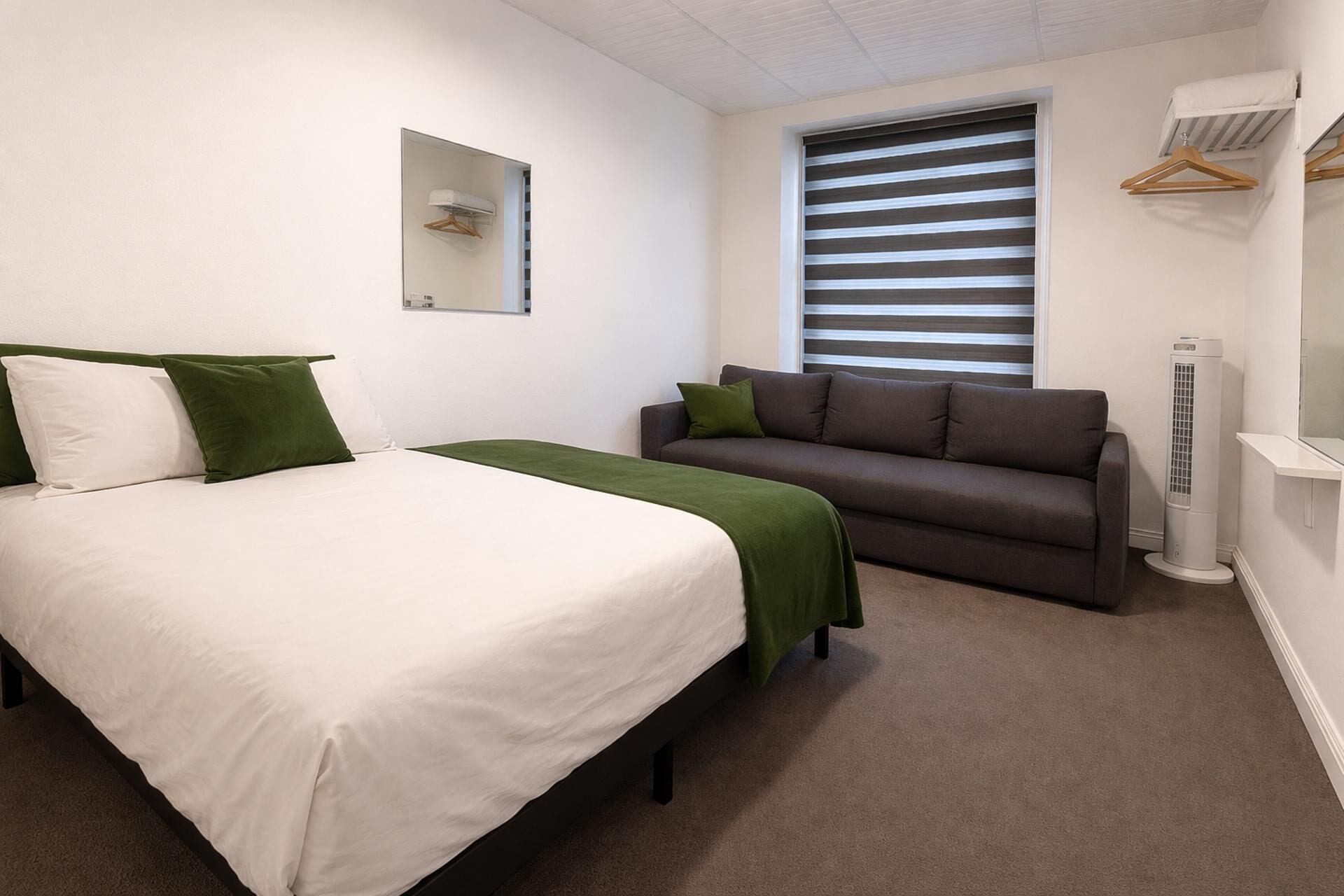 Un dormitorio con cama, sofá, ventana con persianas, unidad de aire acondicionado y un calentador eléctrico.