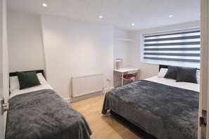 Ein Schlafzimmer mit zwei Betten, einem Heizkörper, einem Schreibtisch mit Stuhl und einem Fenster mit Jalousien.