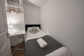 Ein kleines, modernes Schlafzimmer mit Bett, Schreibtisch und Stuhl.