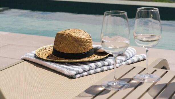 Un entorno junto a la piscina con un sombrero de paja y dos copas de vino sobre una silla, con vista a un viñedo.