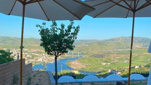 Un patio con un sofá de mimbre, dos sombrillas y vistas a un río y un puente.