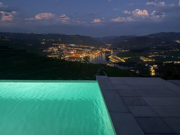 A panoramic view of a city at dusk with a swimming pool in the foreground.