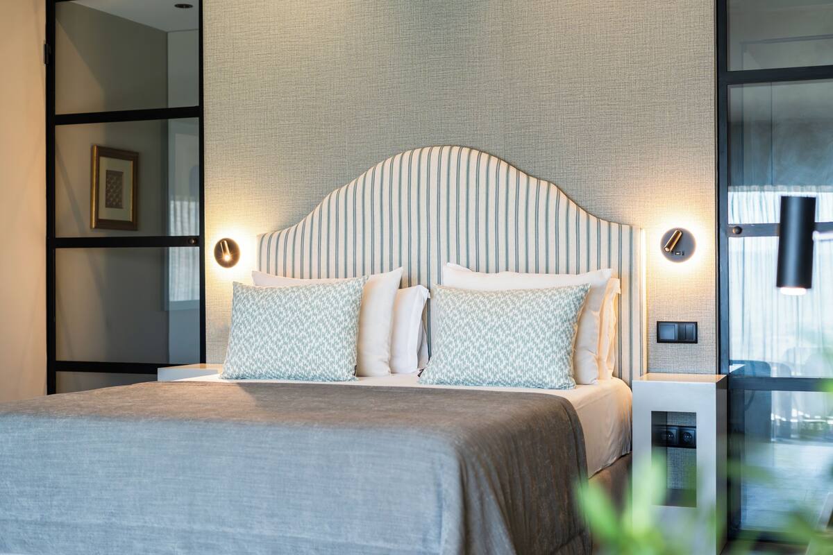 Een moderne slaapkamer met een groot bed, een hoofdbord met verticale lijnen, nachtlampjes en een nachtkastje met een klok.