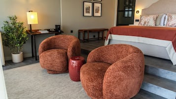 A bedroom with a bed, two armchairs, a small table, a lamp, and a potted plant.