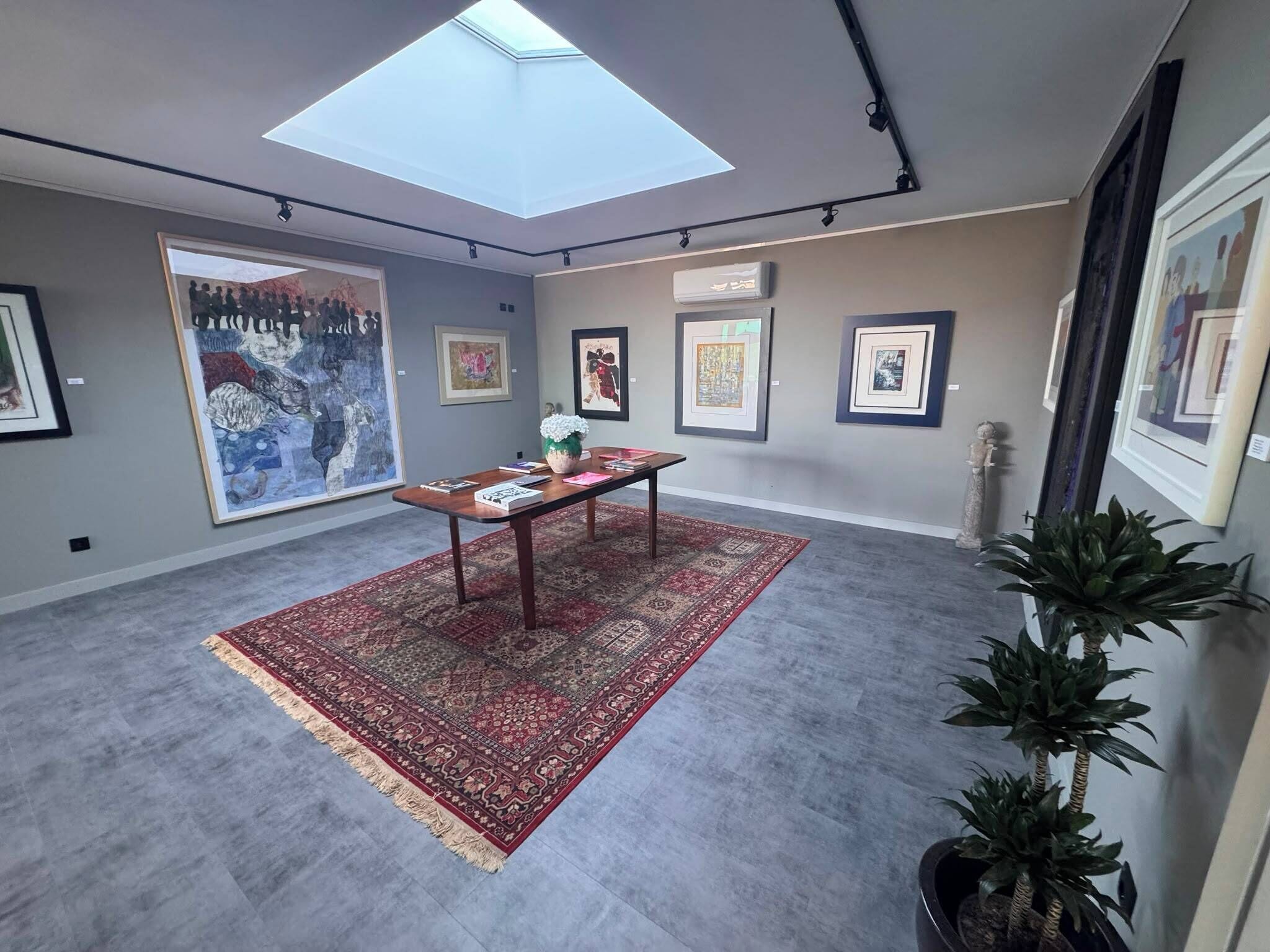 A room with a skylight, a table with books, a patterned rug, and framed artwork on the walls.
