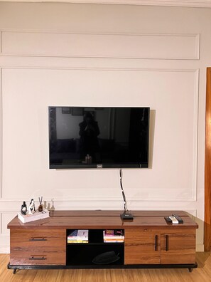 A flat-screen TV mounted on a wall above a wooden entertainment center with drawers and shelves. - Designer 1BHK Apt - Pool, Gym, Sauna Self Checkin' (Rawalpindi)