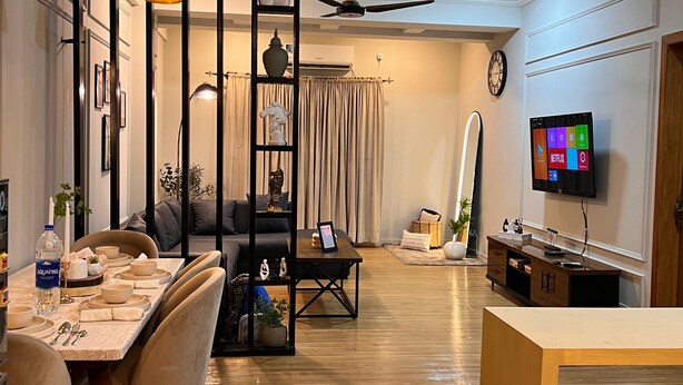 A modern living room with a dining area, a ceiling fan, a flat-screen TV, and a clock on the wall.