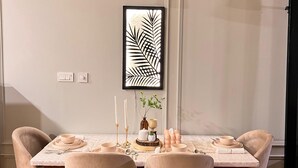 A dining area with a table set for four, featuring a white tablecloth, beige chairs, and black pendant lighting.