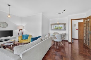 A modern living room with a sofa, TV, and dining area. - Sea Breeze Pilar (Funchal)