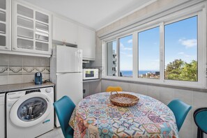 A kitchen with a washing machine, a microwave, and a view of the sea. - Sea Breeze Pilar (Funchal)