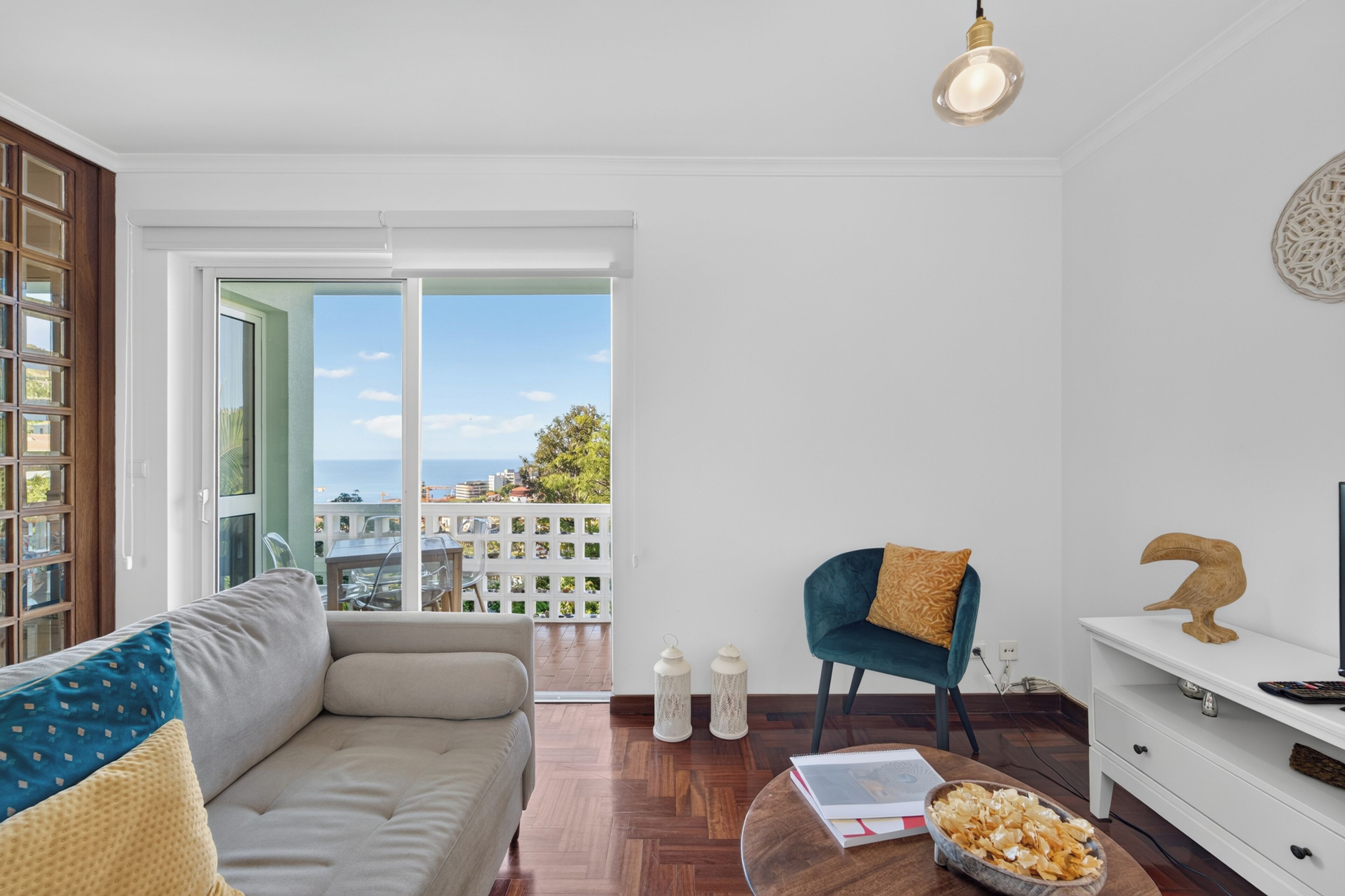 Una sala de estar moderna con un sofá, un sillón, una mesa de centro con aperitivos, un mueble para televisión y vistas al mar a través de amplias ventanas.