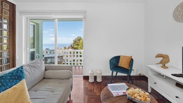 Un soggiorno moderno con un divano, una poltrona, un tavolino da caffè con degli snack, un mobile TV e vista mare attraverso ampie finestre.